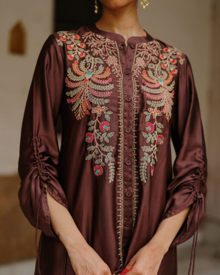 Close-up of a woman in a deep brown silk-blend co-ord set with multicolored floral and paisley embroidery cascading from the mandarin collar, featuring drawstring ruched sleeves.